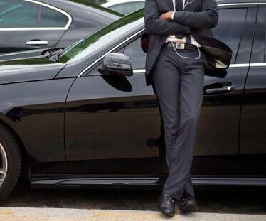 Chauffeur en costume appuyé contre une berline noire
