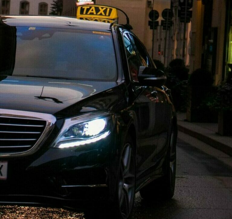 Berline noire avec enseigne lumineuse TAXI, photographiée de nuit