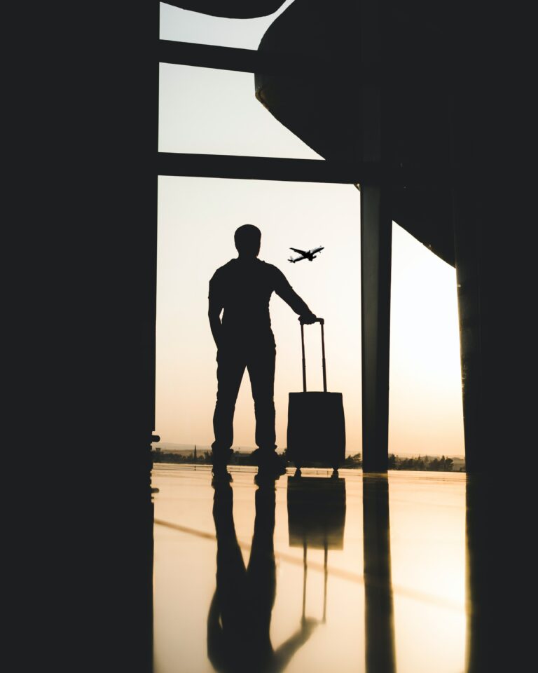 Voyageur avec sa valise devant la baie vitrée d’un aéroport, un avion au décollage